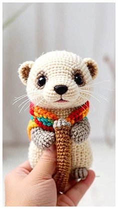 a hand holding a small crocheted animal with a scarf around it's neck