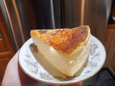 a piece of cheesecake on a plate in front of a stove top oven with someone holding it