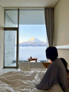 a woman sitting on top of a bed in front of a window with a mountain view