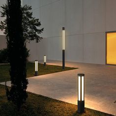 some lights that are in the grass near a building at night with one light on