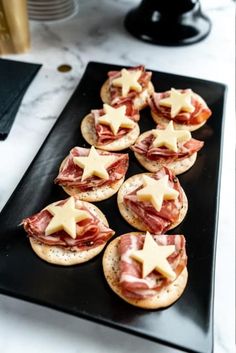 small appetizers with meat and cheese are arranged on a black platter, ready to be eaten