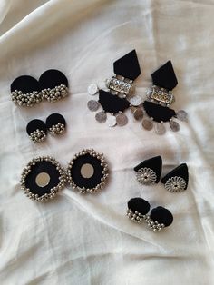 six pairs of black and silver earrings on a white sheet with coins in the background