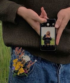 a person standing in a field holding a cell phone up to their chest and taking a selfie