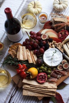 an assortment of cheeses, crackers, and fruit on a table with wine