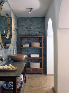 a bathroom with stone walls and flooring is shown in this image, there are shelves on either side of the bathtub