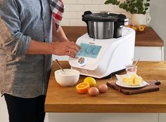 a person standing in front of an electric juicer on a counter with eggs and oranges