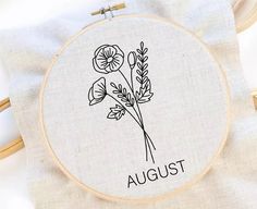 an embroidery project with the word august written in black ink on it and three flowers