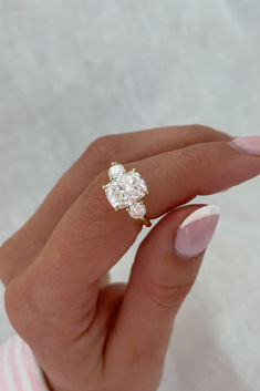 a woman's hand holding an engagement ring with two diamonds on it and pink fingernails