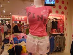 a woman's pink shirt and shorts are on display in a clothing store while people walk by