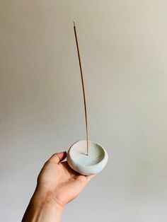 a hand holding a small white bowl with a toothpick sticking out of it