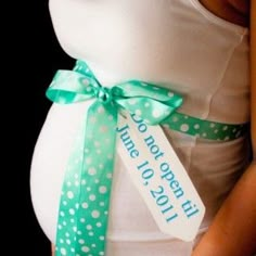 a pregnant woman wearing a white tank top and green polka dot ribbon around her waist