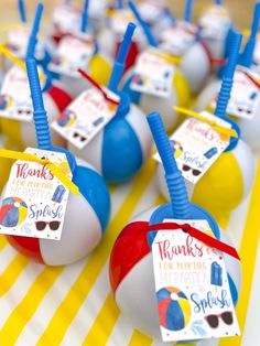 there are many beach balls on the table with name tags attached to them and some strawberries sticking out of them