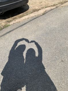 the shadow of a person making a heart with their hands on an asphalt surface next to a parked car