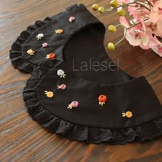 three pieces of black cloth with small flowers on them sitting next to a pink flower vase