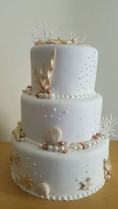 a three tiered wedding cake with seashells and pearls