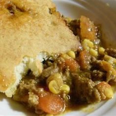 a white plate topped with a piece of pie covered in meat and veggies