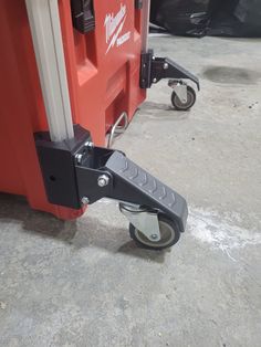 a close up of a red and black cart with wheels on concrete floored area