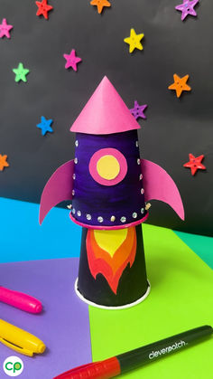 a paper hat with a rocket ship on it and crayons next to it