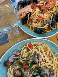 two plates of pasta with clams and mussels on the side next to a glass of wine