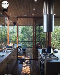 an open kitchen with wood floors and ceiling lights above the stove top oven is surrounded by windows that look out onto trees