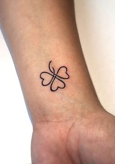 a small four leaf clover tattoo on the left inner wrist, with an arrow in the middle