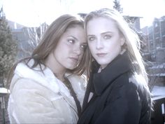 two beautiful young women standing next to each other in front of snow covered trees and buildings