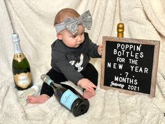 a baby sitting on the floor next to bottles of wine and a sign that says poppin bottles for the new year