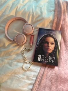 a book, headphones and necklace laying on a bed