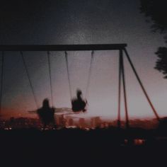 two people on swings at night with city lights in the background and dark clouds overhead