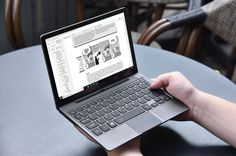 a person is using a laptop computer on a table with chairs in the back ground