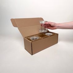 a person is holding a glass in a box with two jars inside and one empty