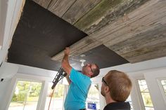 two men working on a ceiling in a room with wood paneling and white walls