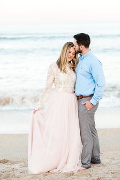 a man and woman standing next to each other on the beach in front of the ocean