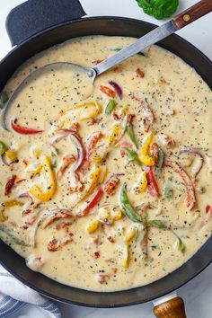 a skillet filled with cheese and vegetables on top of a white table next to a wooden spoon