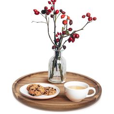 a glass vase filled with red berries next to a white cup and cookie on a wooden tray