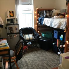 a dorm room with bunk beds, desk and chair in front of a window filled with lights