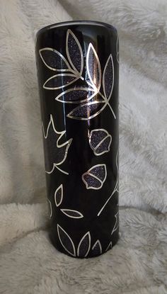 a black coffee cup with white leaves and glitters on the bottom is sitting on a furnishing