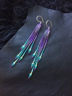 purple and green beaded earrings with gold hooks on black furnishing, close up