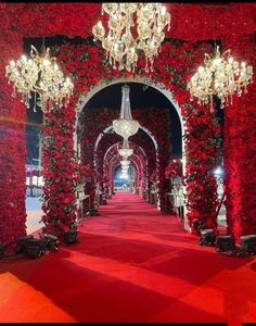 a red carpeted walkway with chandeliers and roses on the walls at night