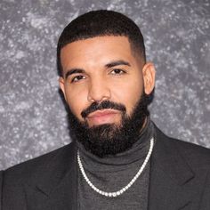 a man with a beard wearing a black suit and silver chain around his neck is looking at the camera