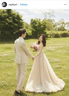 a man and woman in formal wear holding hands while standing in the middle of a field