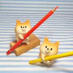 two small cats holding pencils on top of a wooden block