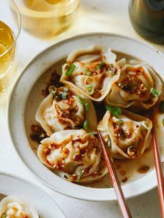 some dumplings are in a white bowl with chopsticks next to them and two glasses on the table