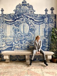 a woman is sitting on a bench in front of a blue and white tile wall