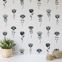 a white table topped with a potted plant next to a wall covered in black flowers