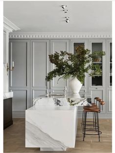 a kitchen with marble counter tops and stools in front of the island, surrounded by gray cabinets