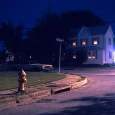 a yellow fire hydrant sitting on the side of a road next to a white house