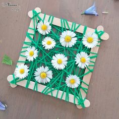 some white daisies are on a green string art project that is made out of wood