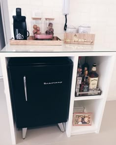 a black refrigerator freezer sitting inside of a kitchen next to a shelf filled with bottles