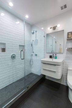 a bathroom with a toilet, sink, and shower stall in white brick wall tiles